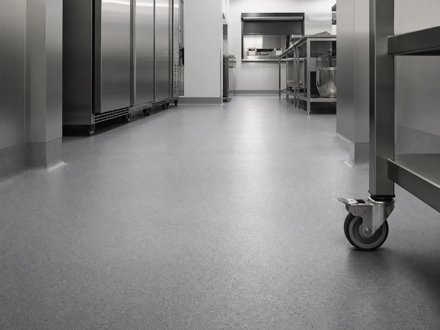 Clean grey resin floor, coved wall base and trolley castor in a commercial kitchen prep corridor