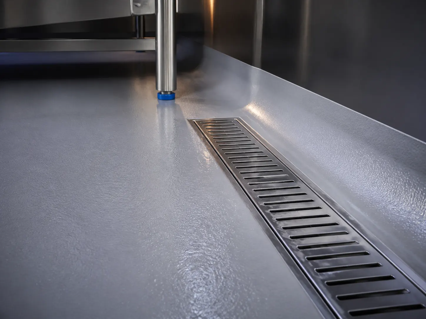 Close technical view of seamless food-production resin floor meeting a stainless trench drain and coved wall base