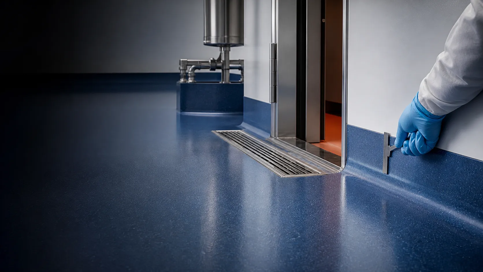 Technician inspecting coved wall junction, stainless drain and doorway termination on a hygienic resin floor